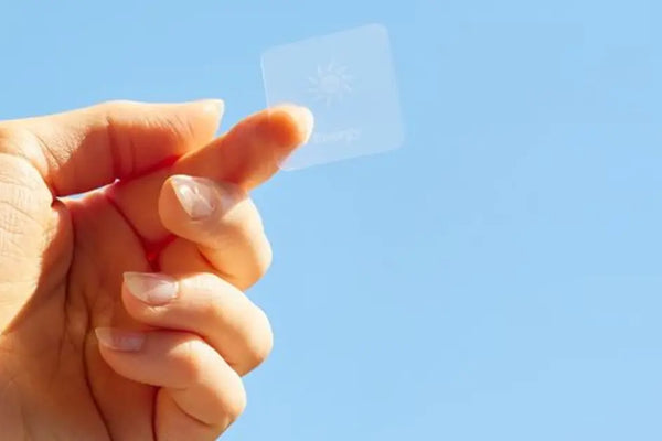 Hand holding a translucent melatonin sleep patch against a clear blue sky background
