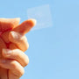 Hand holding a translucent melatonin sleep patch against a clear blue sky background